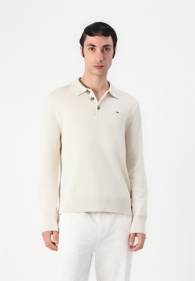 Beige kootud pullover polo kaelusega, kolme pruunist nupuga ning ribidega mansetid ja allääres. Väike logode detail vasakul rinnal.