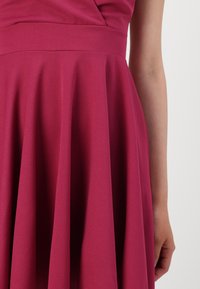 Robe fuchsia avec un corsage ajusté et une jupe évasée. Fabriquée en tissu lisse, avec une taille froncée et des plis subtils.