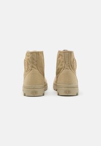 Botas de tobillo de lona beige con una superficie texturizada, suelas de goma y un detalle de logo circular en el talón.
