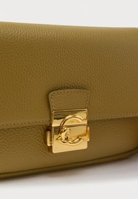 Borsa a mano in pelle verde oliva con una texture liscia, caratterizzata da una chiusura metallica dorata dal design curvo e dettagli cuciti lungo i bordi.