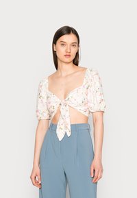 Top cropped floral com mangas bufantes, apresentando um laço à frente e padrão floral em cores pastel. Combinado com calças de cintura alta em azul claro.