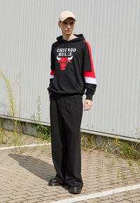 Felpa nera con il logo "Chicago Bulls" e accenti rossi sulle maniche, abbinata a pantaloni neri larghi e scarpe platform nere.
