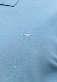 Jasnoniebieska koszulka polo wykonana z textured materiału z małym, wyszywanym logo konia po lewej stronie. Klasyczny krój kołnierzyka.