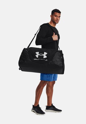 Zwarte duffelbag met groot wit Under Armour-logo, duurzaam materiaal, ronde vorm, uitgerust met een schouderband en stevige handvatten.