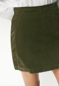 Minirock aus olivgrünem Cord mit vertikaler Rippung, tailliertem Bund und sauberem Saum. Geeignet für legere Anlässe.