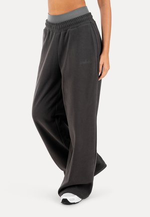 Luźne ciemnoszare spodnie dresowe z elastycznym paskiem w talii i bocznymi kieszeniami, noszone z białymi butami sportowymi.