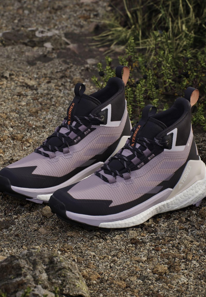 Męskie wysokie buty do biegania w terenie z czarną i liliową siateczkową cholewką, teksturowanym wykończeniem, białą podeszwą środkową oraz wzmocnioną czarną gumową podeszwą.