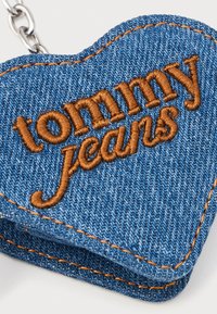 Farmer szív alakú kulcstartó, barna hímzéssel "tommy jeans" felirattal, látható varrással és ezüstszínű fém lánc csatlakozással.