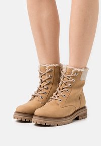 Botines de ante marrón con forro de pelo sintético, ojales de metal y diseño con cordones. Presentan una suela de goma resistente y suaves acentos de tela.