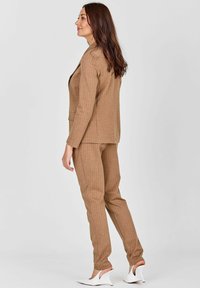 Pruun ribaülese ülikond kohandatud pintsakuga ja kitsaste pükstega. Kangas on sileda tekstuuriga; kombineeritud valgete kontsakingadega.