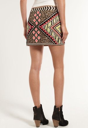 Kobieta ubrana w krótką spódnicę z geometrycznymi wzorami w kolorach czerwonym, żółtym i czarnym, w połączeniu z czarnymi botkami na obcasie.