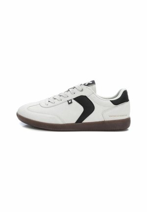 Zapatillas de ante blancas con un acento curvado negro, cordones grises, suela de goma marrón y un logotipo negro en contraste en la lengua.