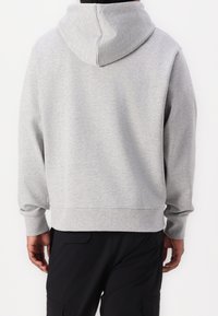 Grå huvtröja med en mjuk textur, ribbade ärmar och en tät midja, visad bakifrån mot en neutral bakgrund.