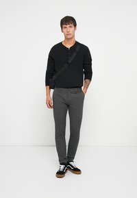 Camiseta negra de manga larga acanalada, pantalones gris slim-fit y zapatillas negras con cordones blancos y suelas marrones. Diseño simple, colores neutros.