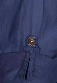 Tissu bleu marine à texture lisse avec une fermeture à bouton marron, patte de boutonnage cousue et un design épuré et simple.