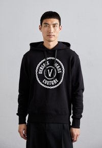 Felpa nera in tessuto morbido con una grafica centrale bianca contenente il testo "Versace Jeans Couture" e un design a catena. Con cappuccio regolabile.