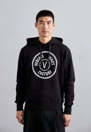 Felpa nera in tessuto morbido con una grafica centrale bianca contenente il testo "Versace Jeans Couture" e un design a catena. Con cappuccio regolabile.