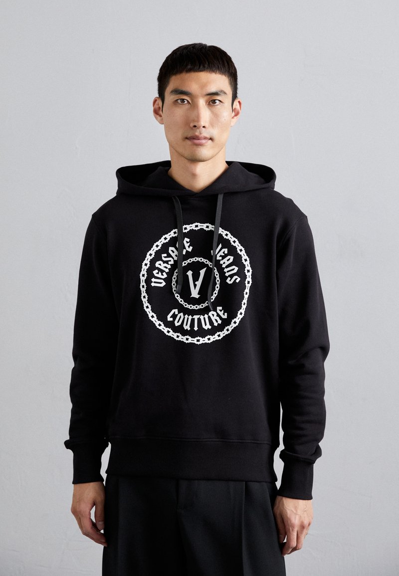 Felpa nera in tessuto morbido con una grafica centrale bianca contenente il testo "Versace Jeans Couture" e un design a catena. Con cappuccio regolabile.