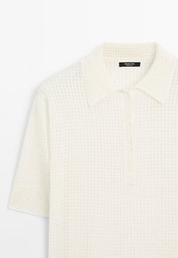 Witte polo met korte mouwen, voorzien van een gemêleerd breipatroon, knoopsluiting en een klassieke kraag. Lichtgewicht stof met een ademend ontwerp.