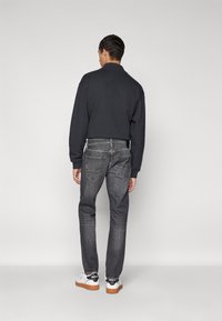 Temno siva pulover, fit slim jeans in bele superge z črnimi detajli. Teksturirana tkanina in vidni krojaški detajli na trapericah.