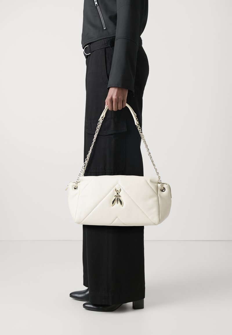 Borsa bianca trapuntata con un'accattivante decorazione di insetto dorato, tracolla a catena, forma rettangolare e superficie liscia, tenuta da una persona in abbigliamento nero.
