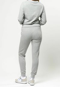 Grå bomullströja och matchande joggers med ribbade muddar och midja. Bärs med vita och grå sneakers. Slät textur, avslappnad design.