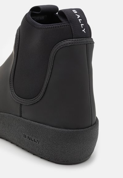 Boots negre înalte cu un exterior din piele netedă, panouri laterale elastice și o talpă din cauciuc texturată, având un tab de prindere etichetat "BALLY."