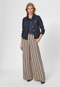 Marineblauwe spijkerjacket met voorzakken en zilveren knopen, gecombineerd met beige wijde broek met marineblauwe verticale strepen.