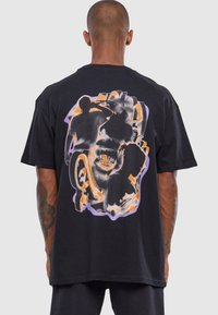 Black cotton t-shirt featuring a colorful graphic print on the back, showcasing abstract human silhouettes with orange and purple accents.
