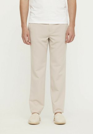 Pantalons beiges à coupe droite, en tissu léger, avec une texture subtile et des poches latérales. Associés à des chaussures beige à enfiler.