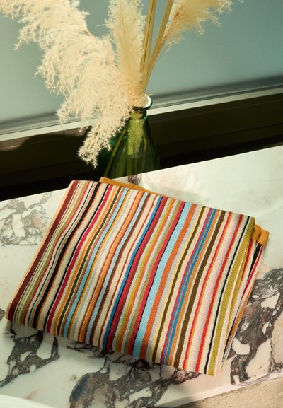 Multicolored striped textile featuring bold hues of red, blue, yellow, and green, with a textured surface, folded on a marble background.