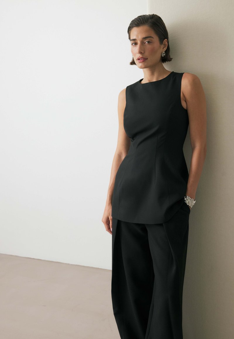 Musthave kaeluseta topp, millel on tihe kehaosa ja kerge flare, koos laia jala pükstea. Sujuv kangas ja minimalistlik disain.