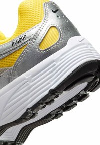 Die Nike P-6000 Sneakers verfügen über ein silbernes Obermaterial mit gelben Mesh-Akzenten, eine strukturierte schwarze Gummisohle und ein geschichtetes Design mit kontrastierenden Materialien.