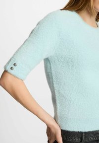 Maglione azzurro chiaro, morbido e felpato, con scollatura rotonda e maniche corte, che presenta due bottoni decorativi sul polsino. Texture morbida e design aderente.