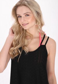 Top nero senza maniche con dettagli a taglio, sovrapposto a una fascia rosa, con scollatura rotonda e tessuto testurizzato. Orecchini a cerchio notevoli.