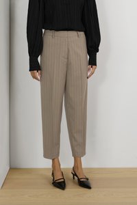 Pantalons beiges à rayures fines avec une coupe ajustée, ourlet retroussé et poches latérales. Portés avec un haut noir texturé à manches longues et des talons noirs.