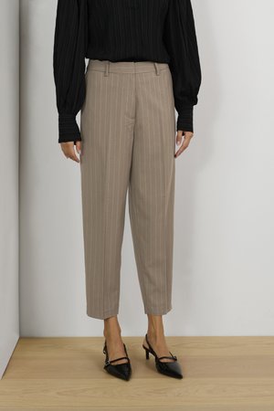 Beige, celana bergaris dengan potongan yang disesuaikan, ujung berkancing, dan saku samping. Dipakai dengan atasan hitam berbahan tekstur lengan panjang dan sepatu hak hitam.