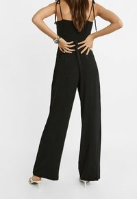 Zwarte jumpsuit met een nauwsluitend gerimpeld lijfje, broek met wijd uitlopende pijpen en verstelbare bandjes. Soepele stof, minimalistisch ontwerp, geen zichtbare patronen.