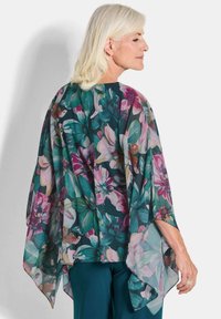 Floraal kimono-stijl top in doorzichtig materiaal, met grote roze en groene bloemen op een donkerblauwe achtergrond, brede mouwen en een asymmetrische zoom.