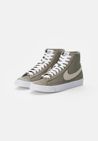 Höga sneakers i olivgrön tyg med vita snören och en texturerad grå swoosh. Har en vit gummisula och vadderad krage.