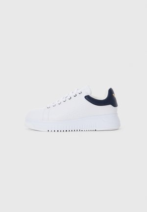 Baskets blanches avec des accents navy, présentant une texture lisse, un bout rond et une semelle surélevée, ornées d'un logo sur le côté.