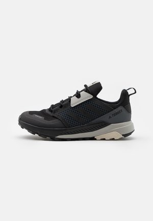 Zapatilla deportiva negra con parte superior de malla y sintético, presenta detalles en gris, suela con textura y un diseño estable y acolchado.
