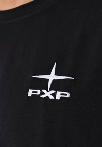 Camiseta de algodón negra con un destacado logo bordado en blanco que presenta una estrella y el texto "PXP" en el frente. Textura suave, manga corta.