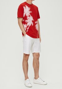 T-shirt rouge à manches courtes avec imprimé de palmier blanc, associé à un short blanc et des baskets blanches, avec un col rond.