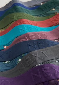 Pinotut värikkäät kangasvyöt, joissa on painettu sana "NEXT", ja alla näkyvissä erilaisia kangaskuvioita.