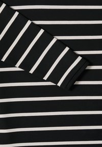 Materiał w paski czarno-białe z poziomymi liniami. Tkanina wydaje się miękka i dziana. Posiada złożony rękaw z wyraźnymi kontrastowymi paskami.