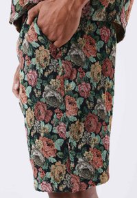 Shorts fleuris en tissu texturé, présentant un fond noir et des motifs de roses colorés en rouge, orange, vert et beige.