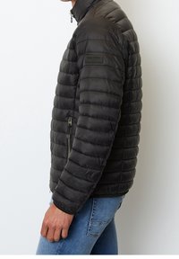 Sort pufferjakke lavet af letvægtsmateriale, med vandret quiltet mønster, høj krave og lynlåslomme på siden.