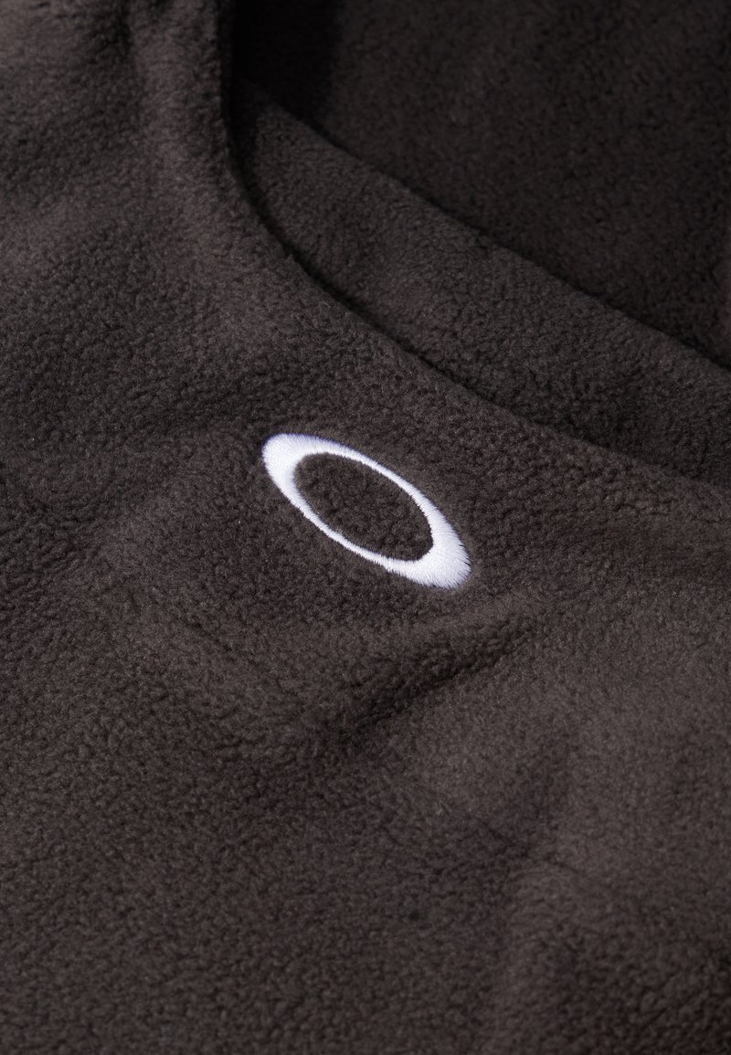 Brauner Fleece-Stoff mit einem auffälligen weißen runden Logo. Weiche Textur mit leichtem Glanz, die Tiefe in Falten und Knicken zeigt.