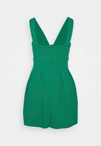 Grön klänning med V-ringning, breda band, plisserad kjol och dold dragkedja i ryggen. Tillverkad av ett slätt tyg med en matt yta.